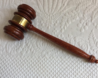 Op de afbeelding: Een houten hamer met een messingband rond de kop. De hamer heeft een donkerbruine afwerking en een afgeronde handgreep.