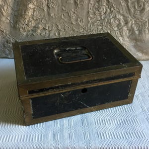 Vintage Cash Box in Black with Gold Brass Borders All Around. Handle on Top of Box. There is no lock or latch. Great for Display or Storage.