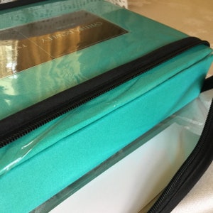 Peut inclure: Un sac de rangement zippé bleu turquoise avec une fenêtre en plastique transparent montrant le texte "California Downy" sur un fond blanc.