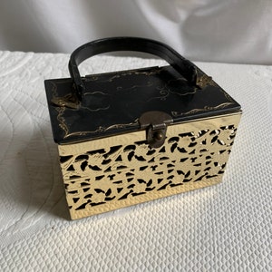 Peut inclure: Un sac à main vintage noir et or avec un motif découpé et une poignée en cuir noir.