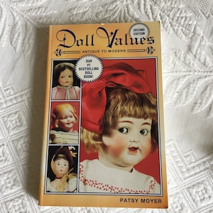 Peut inclure: Un livre intitulé "Doll Values: Antique to Modern" avec un nœud rouge et un visage de poupée sur la couverture. Le livre est notre best-seller de livres sur les poupées.