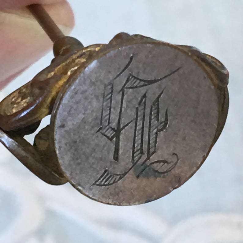 May include: Antique brass seal with a wooden handle and a circular metal stamp with the engraved initials "HF".