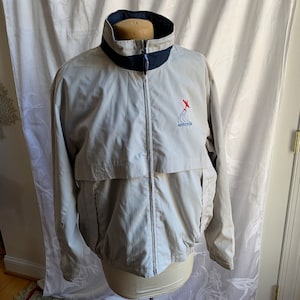May include: A light gray windbreaker jacket with a blue and white striped collar and a zipper closure. The jacket has a logo on the left chest that says "Aerocosta" with a red airplane graphic.