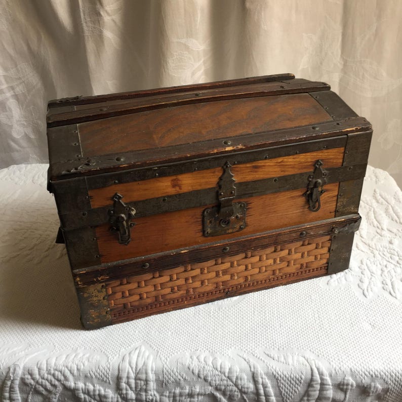 Puede incluir: Un cofre de madera vintage con un fondo de mimbre tejido y detalles met&aacute;licos. El cofre tiene una tapa con bisagras y una cerradura.