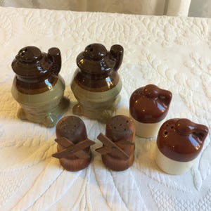 Puede incluir: Conjunto de seis saleros y pimenteros vintage de cerámica. Los saleros tienen forma de jarra, estufa y zueco de madera. Los saleros son marrones, blancos y beige.