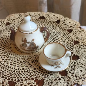 Vintage 4 Piece Teapot w/ Lid, Cup and Saucer. White Porcelain with Gold Accents. Picture of French Colonial Man and Woman on Teapot.