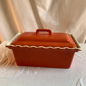 May include: Orange ceramic baking dish with a lid and scalloped edge. The dish has a handle on the lid.