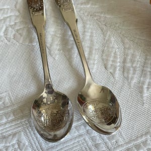 May include: Two silver spoons with the seal of the State of Delaware on the front. The spoons are on a white tablecloth.
