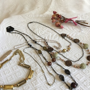May include: Five different necklaces with various materials and styles. The necklaces include gold chains, brown wooden beads, and black and brown beads.