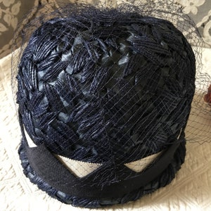 May include: A navy blue hat with a woven texture and a white trim. The hat is covered in a fine mesh veil.