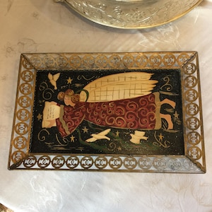 May include: A gold metal tray with a decorative cutout border. The tray features a painted image of an angel with wings, holding a scroll and surrounded by doves. The background is black with gold stars.