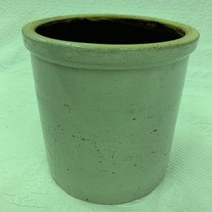 Pode incluir: Um pote de cerâmica branco com uma borda marrom. O pote tem uma superfície texturizada e está ligeiramente desgastado.