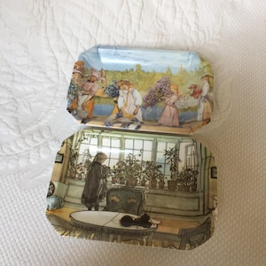 May include: Two rectangular trays with a white background and a floral design. The top tray features a group of people picking flowers in a garden. The bottom tray features a woman tending to plants in a greenhouse.