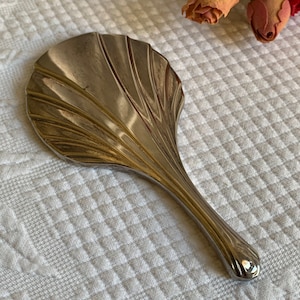 Espejo de mano pequeño vintage Art Déco. Acabado plateado con líneas decorativas ligeramente curvadas en la parte posterior. Un encantador espejo de mano pequeño.