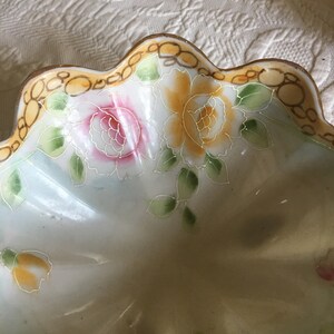 May include: A white porcelain bowl with a scalloped edge and a floral design. The bowl is decorated with yellow, pink, and green flowers.