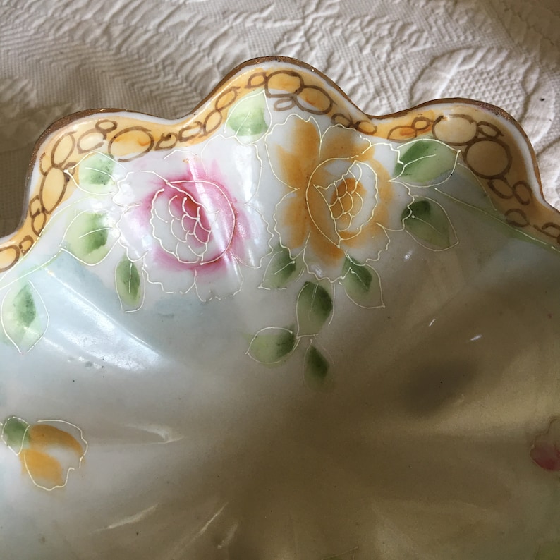 May include: A white porcelain bowl with a scalloped edge and a floral design. The bowl is decorated with yellow, pink, and green flowers.
