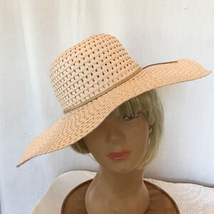 May include: A wide-brimmed straw hat with a woven design and a brown ribbon. The hat is light pink in color.