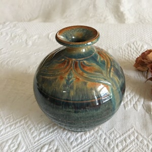 May include: A small, round, blue and brown ceramic vase with a wide mouth and a textured design.
