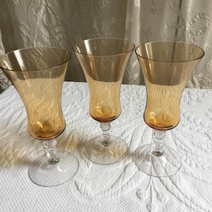 May include: Set of three amber glass stemmed drinking glasses with a flared bowl and a clear glass base.