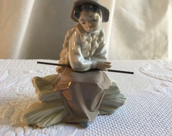 Vintage 1990 Figura de porcelana Lladró de niña sentada sobre un montón de heno con palo en la mano y sombrero en la cabeza. Usando chaleco largo con bolso.