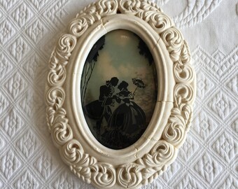 Pintura vintage de siluetas de sombras sobre vidrio abovedado. Marco ovalado de yeso estilo shabby chic. Pareja romántica en silueta contra el cielo. Preciosa.