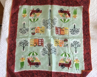 Op de afbeelding: Een groen en wit katoenen zakdoek met een rode rand. De zakdoek heeft een herhalend patroon van kleine huizen, bomen en fruitkarren. Het patroon is in vintage stijl.