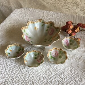 May include: A set of four white porcelain bowls with a scalloped edge and floral design. The bowls are decorated with pink and yellow roses and green leaves. The bowls have a gold trim around the edge.