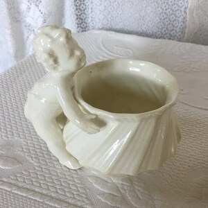 May include: White ceramic planter shaped like a shell with a cherub figure holding the shell. The planter is a vintage style.