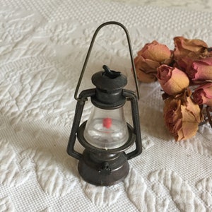 May include: A vintage metal pencil sharpener shaped like a lantern. The sharpener has a clear plastic window and a red pencil lead inside. The lantern has a handle and a metal base.