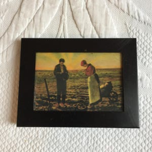 May include: A framed painting depicting two figures in a field. The figures are a man and a woman, both wearing traditional clothing. The man is holding a tool, and the woman is looking down at the ground. The painting is set against a backdrop of a sunset sky.