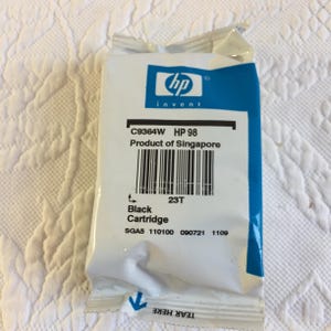 May include: A white and blue HP 98 black ink cartridge in its original sealed plastic packaging. The label displays the text C9364W, HP 98, Product of Singapore, Black Cartridge, and includes a barcode, serial numbers, and a tear here indicator.