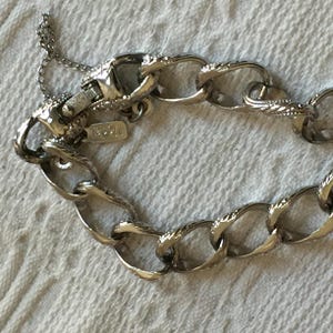 May include: Silver-toned chain bracelet with textured oval links. The bracelet has a lobster clasp closure and a small tag that reads "Monet". The chain is displayed on a white surface.