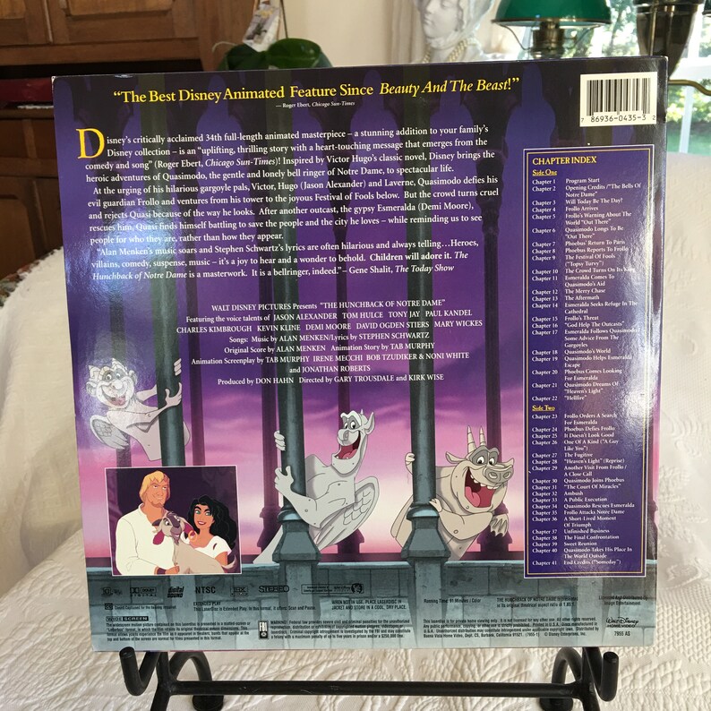 May include: The back cover of a VHS tape for the animated film The Hunchback of Notre Dame. The cover features a scene from the film with Quasimodo, Esmeralda, and the gargoyles. The text on the cover reads "The Best Disney Animated Feature Since Beauty And The Beast!" and includes a chapter index for the film.