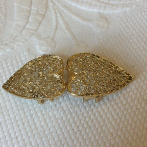 May include: A gold-tone metal heart-shaped belt buckle with a delicate filigree design.