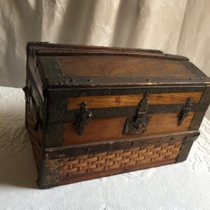 Puede incluir: Un cofre de madera vintage con un fondo de mimbre tejido y detalles met&aacute;licos. El cofre tiene una tapa con bisagras y una cerradura.