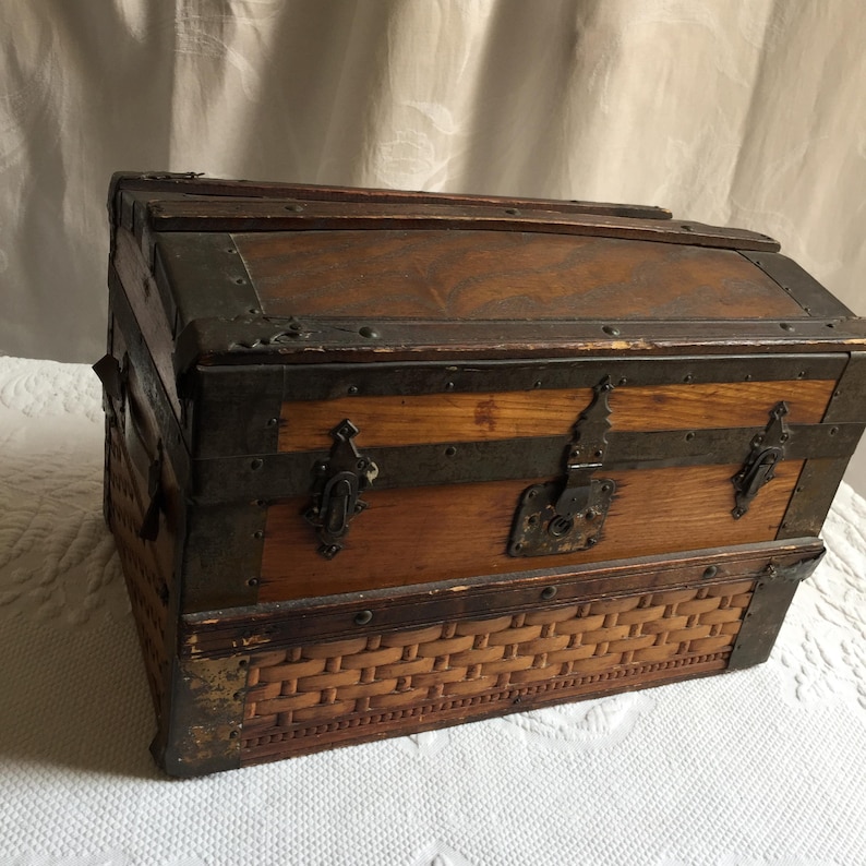Puede incluir: Un cofre de madera vintage con un fondo de mimbre tejido y detalles met&aacute;licos. El cofre tiene una tapa con bisagras y una cerradura.