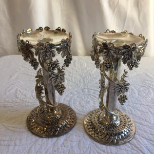 Puede incluir: Un par de candelabros de plata con un diseño de vid. Los candelabros están detallados con hojas y uvas.
