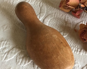 May include: A wooden shoe stretcher in the shape of a bowling pin. The stretcher is light brown and has a smooth, polished finish.