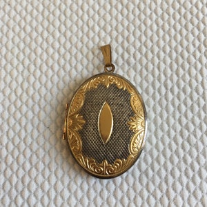 May include: A gold oval locket with an intricate floral design and a small, oval-shaped opening in the center.