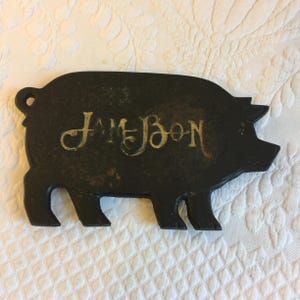 Puede incluir: Un abridor de botellas de hierro fundido negro en forma de cerdo con la palabra "JAMESON" escrita en letras doradas.