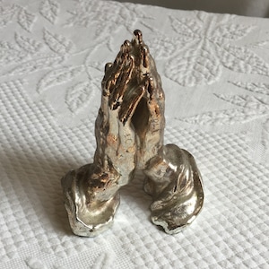 Zabytkowa posrebrzana figurka modlących się rąk. Niebieska flokowana podstawa. Długie cienkie palce i dłonie. Piękne dłonie. Religijne dłonie.