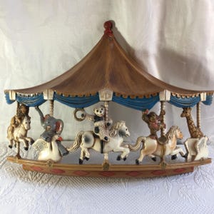 Puede incluir: Una decoración mural con temática de carrusel, con un dosel marrón y beige y adornos azules. El carrusel presenta varias figuras de animales, incluyendo un león, un elefante, un mono, una jirafa y un oso, montados en caballos blancos y beige.