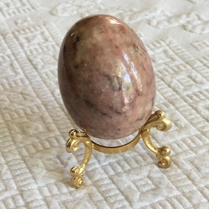 May include: A pink and white marble egg on a gold metal stand. The egg has a swirling pattern of pink and white.