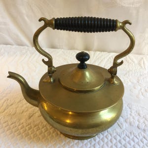 May include: A vintage brass teapot with a black wooden handle and a lid. The teapot has a round body and a spout on the side.