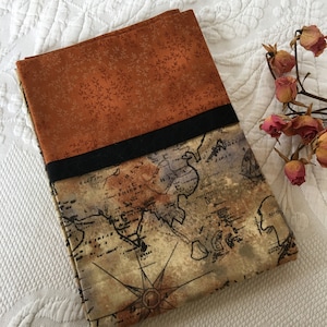 Può includere: Una copertina per libro in tessuto con un motivo floreale arancione nella parte superiore e una mappa del mondo vintage nella parte inferiore. La mappa è stampata in inchiostro marrone e nero su uno sfondo beige. Un nastro nero è cucito sulla parte superiore della copertina.