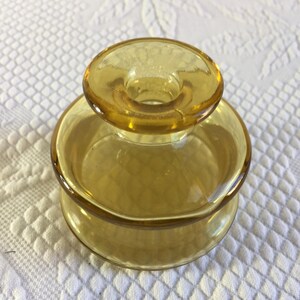 Peut inclure: Un bougeoir vintage en verre ambré. Le bougeoir a une base ronde et un dessus circulaire avec un trou pour une bougie. Le verre est d'une couleur dorée chaude. Le bougeoir est probablement de l'époque du milieu du siècle.