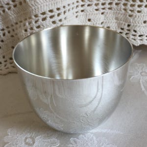 May include: A silver cup with a slightly rounded bottom and a smooth, polished surface. The cup has a subtle embossed design.