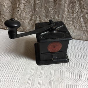 Molinillo de café antiguo. Molinillo Universal Mill n.° 109 de metal negro con puerta de acceso superior y cajón frontal para después de moler. Mango de madera.