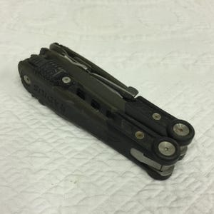 Pode incluir: Uma ferramenta multifuncional preta e verde com a palavra "Radius" impressa no lado. A ferramenta possui várias lâminas e acessórios.