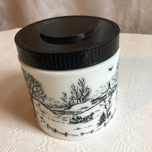 Tarro vintage de vidrio blanco para leche con tapa de plástico negra. El tarro presenta dibujos en negro de trineos tirados por caballos, granjas, iglesias, vallas, árboles y pájaros.